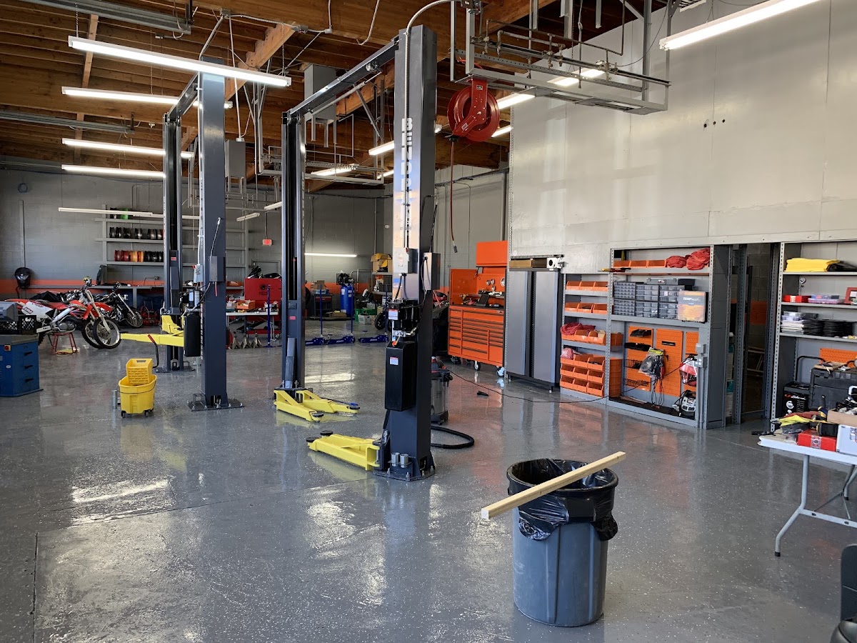 Inside the Palmdale Auto Services workshop, two post lifts, orange tool chests and motorcycles along the wall